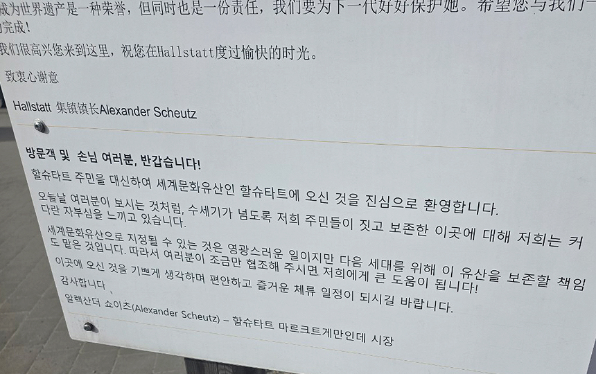 오스트리아 할슈타트에서 여러 언어로 관광객을 환영하고 문화유산 보존을 당부하는 안내문